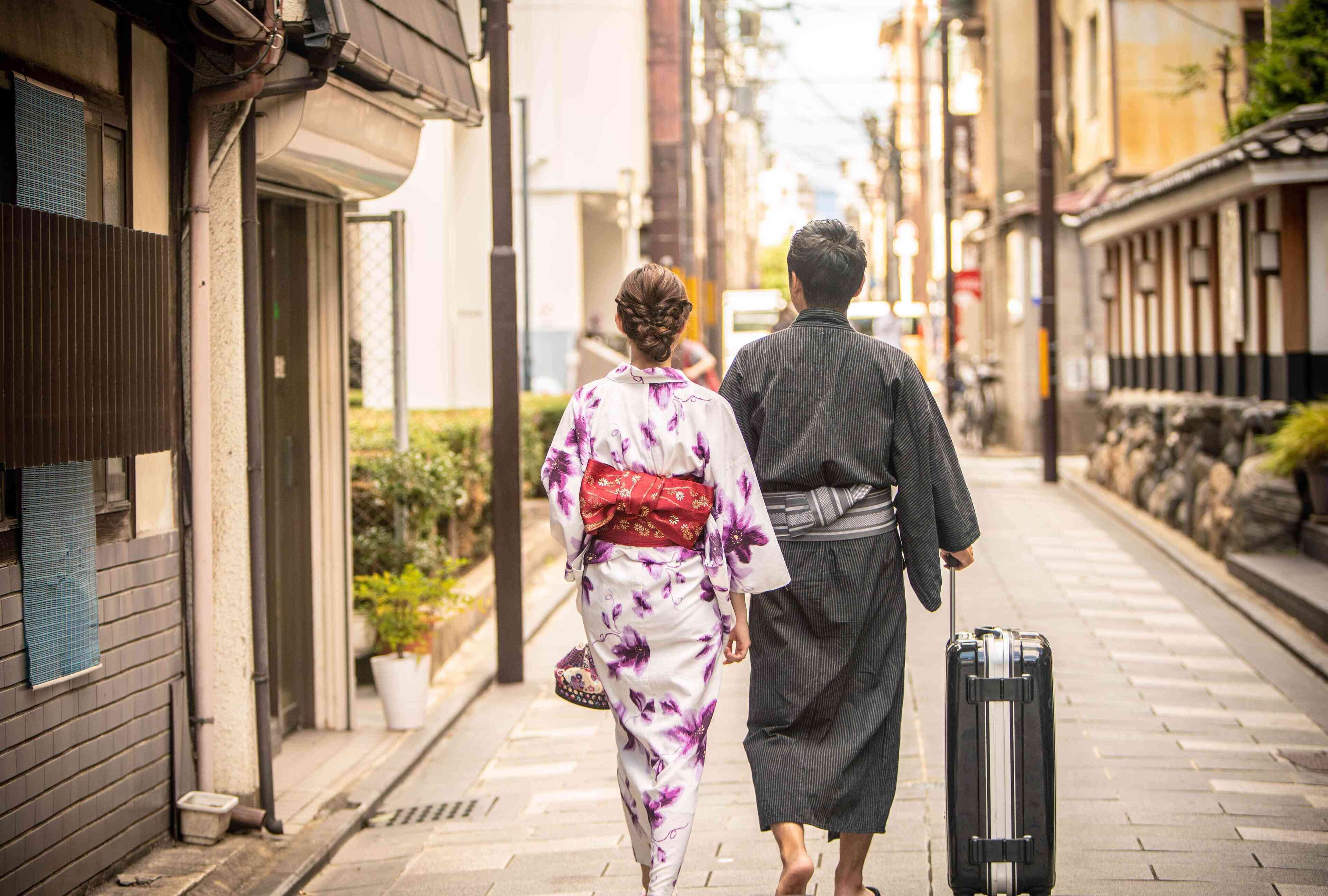 A narrow urban street with traditional buildings, a couple walking, and a suitcase.