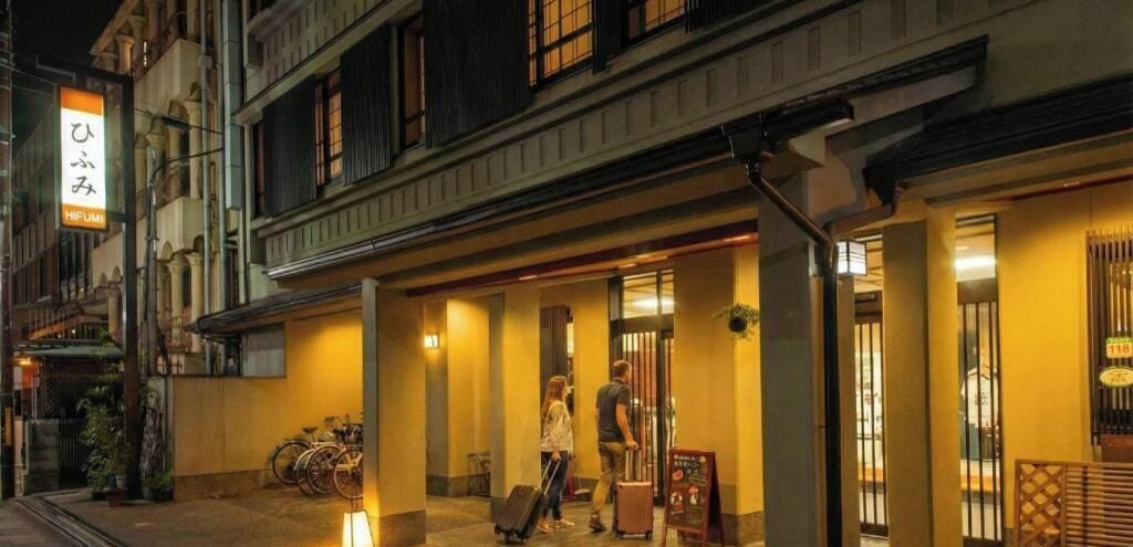 A hotel entrance with a signboard, a bicycle parked outside, and a person carrying luggage.