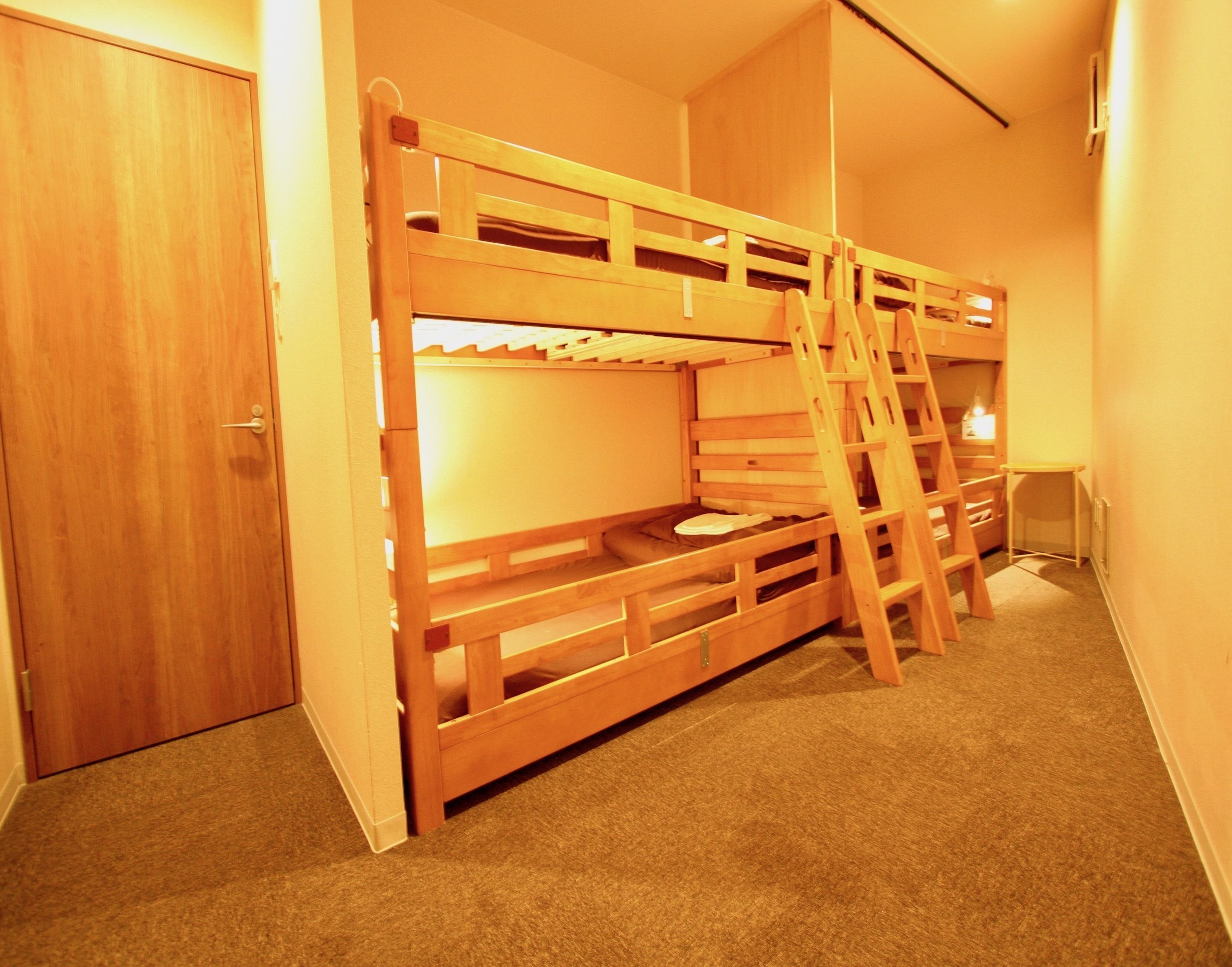 A bunk bed room with a wooden ladder, carpeted floor, and a door.