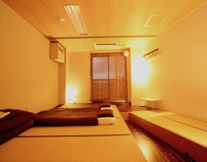 A room with tatami mats, a futon bed, a small table, and a sliding door. - Osaka Guesthouse Nest - Hostel (Osaka)