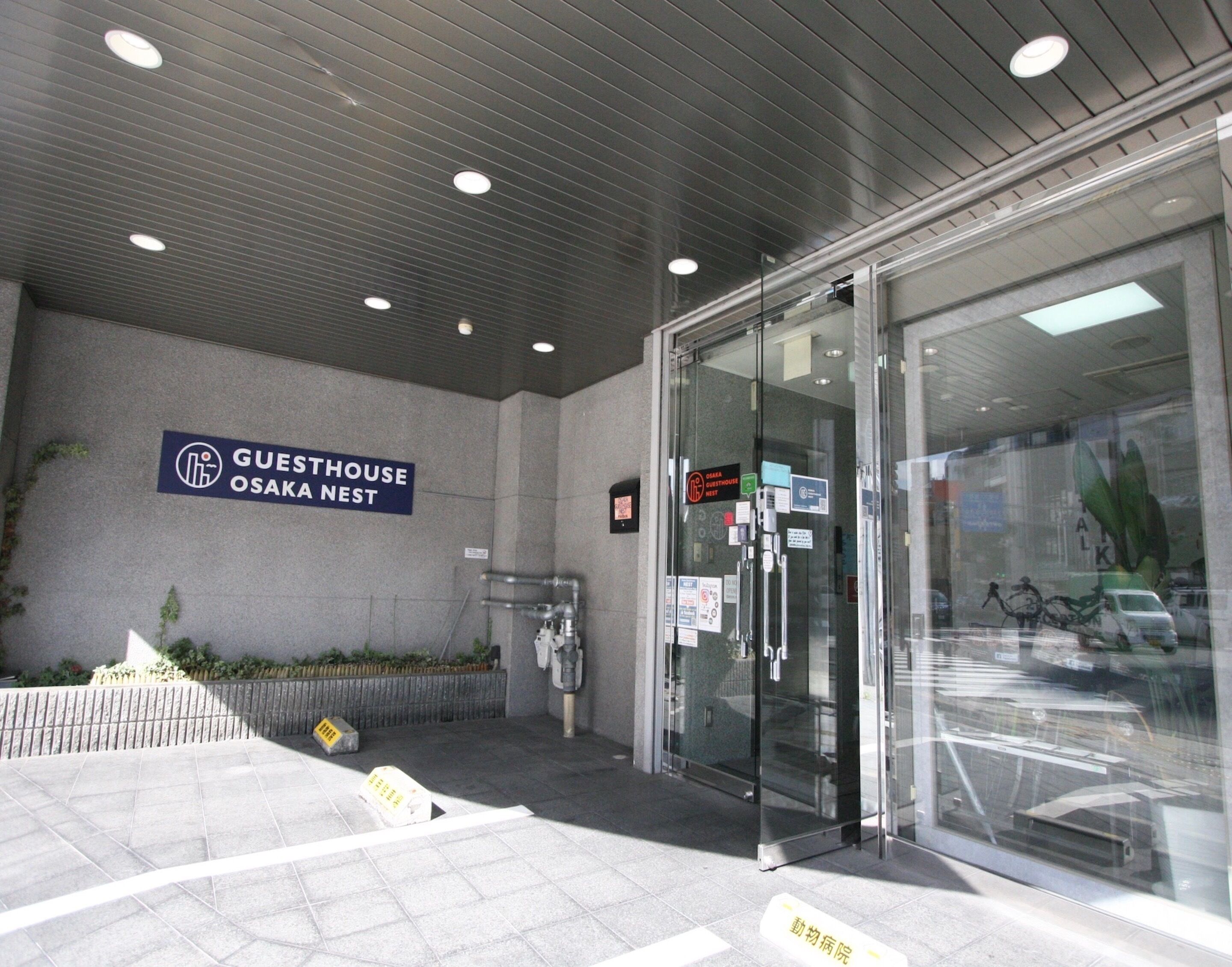 Een hotelentree met een bord waarop staat 'Guesthouse Osaka Nest'.