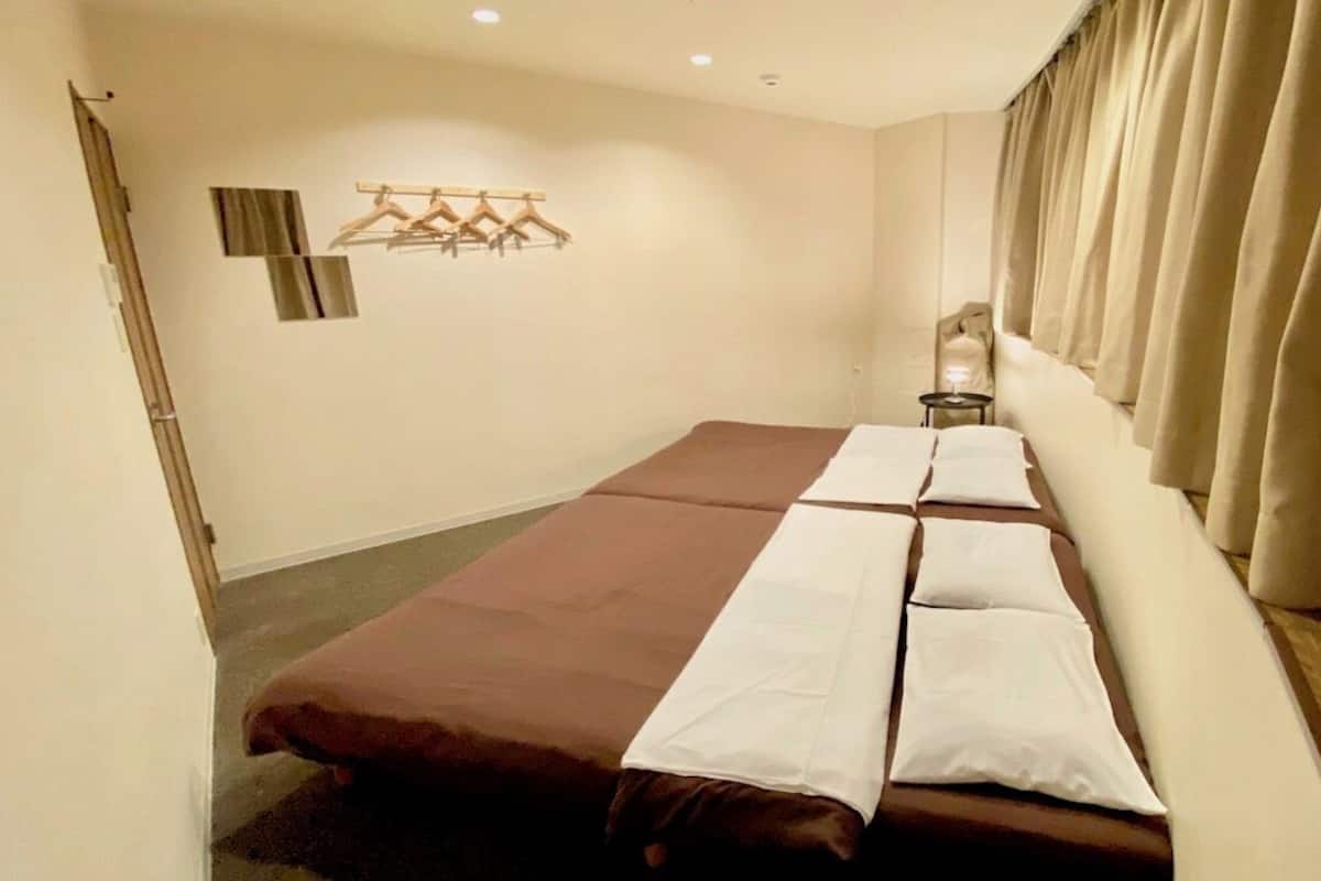 Habitación de hotel con cama, mesita de noche, perchero y ventana con cortinas.