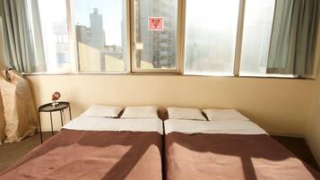 A twin bed room with a large window, a small table with a lamp, and a curtain on the left.