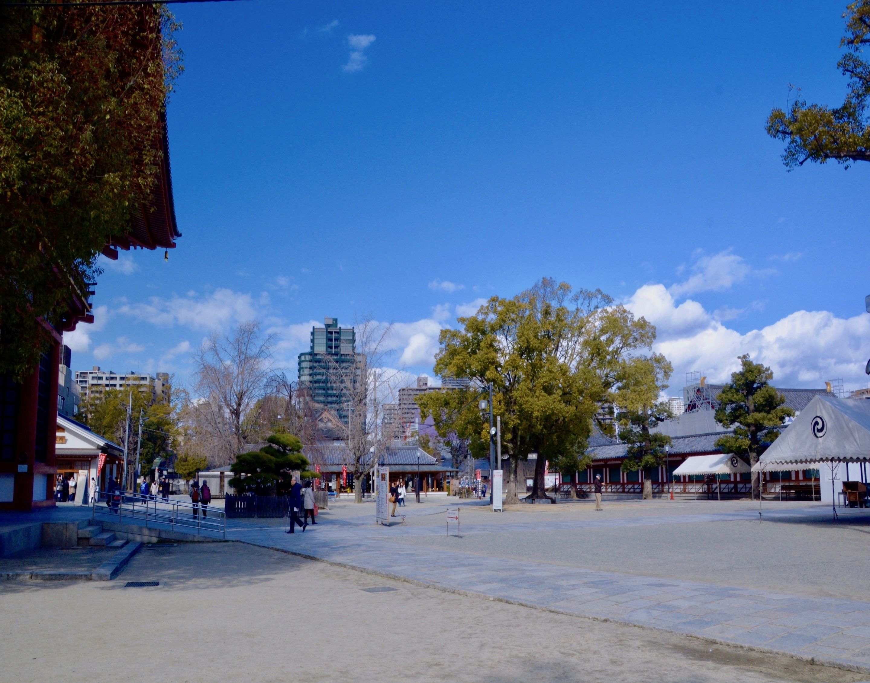 Una amplia plaza pública con edificios tradicionales, un rascacielos moderno al fondo y un cielo azul despejado.