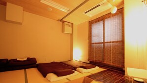 A traditional Japanese-style room with tatami flooring, a low bed, a small table, and a sliding door with a view of the outside. - Osaka Guesthouse Nest - Hostel (Osaka)