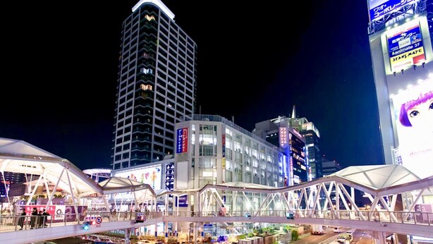 A modern urban area with a prominent high-rise building, a covered pedestrian walkway, and various commercial establishments. - Osaka Guesthouse Nest - Hostel (Osaka)