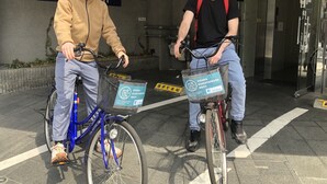 Two individuals on bicycles with baskets, in front of a building with a sign reading "OSAKA GUESTHOUSE NEST". - Osaka Guesthouse Nest - Hostel (Osaka)