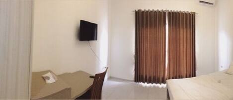 A hotel room with a bed, a desk, a chair, a TV, and a window with curtains.