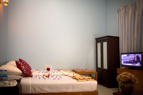 A bedroom with a bed, a television, a cabinet, and a vase with flowers. - Famous Hotel (Pyin Oo Lwin)