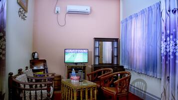 A living room with a television, wooden furniture, a wicker coffee table, and a red carpet.