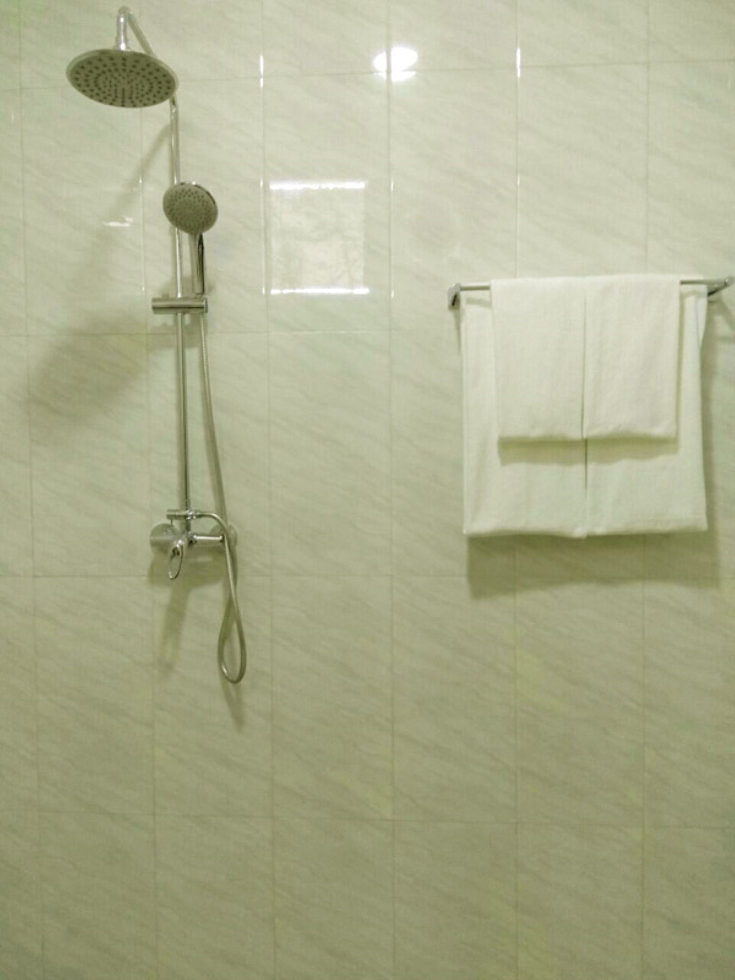 A bathroom with a shower, a towel rack with two towels, and a wall with a tiled pattern.