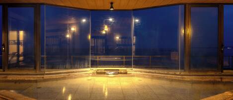 Un área de piscina interior con paredes de vidrio, un accesorio de luz central y un borde de piedra.