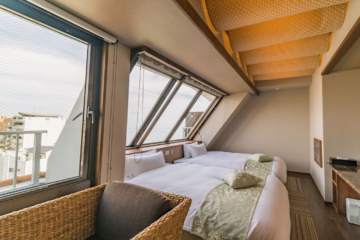 A hotel room with a large window, a bed, a TV, and a desk.