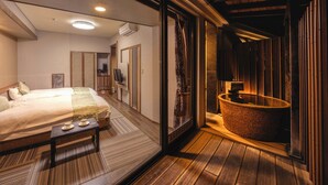 A modern hotel room with a large bed, a wooden floor, a bathtub, and a small table with cups.