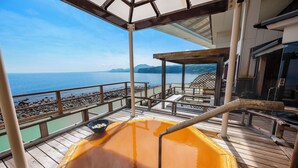 A hot tub on a wooden deck with a view of the sea and mountains.