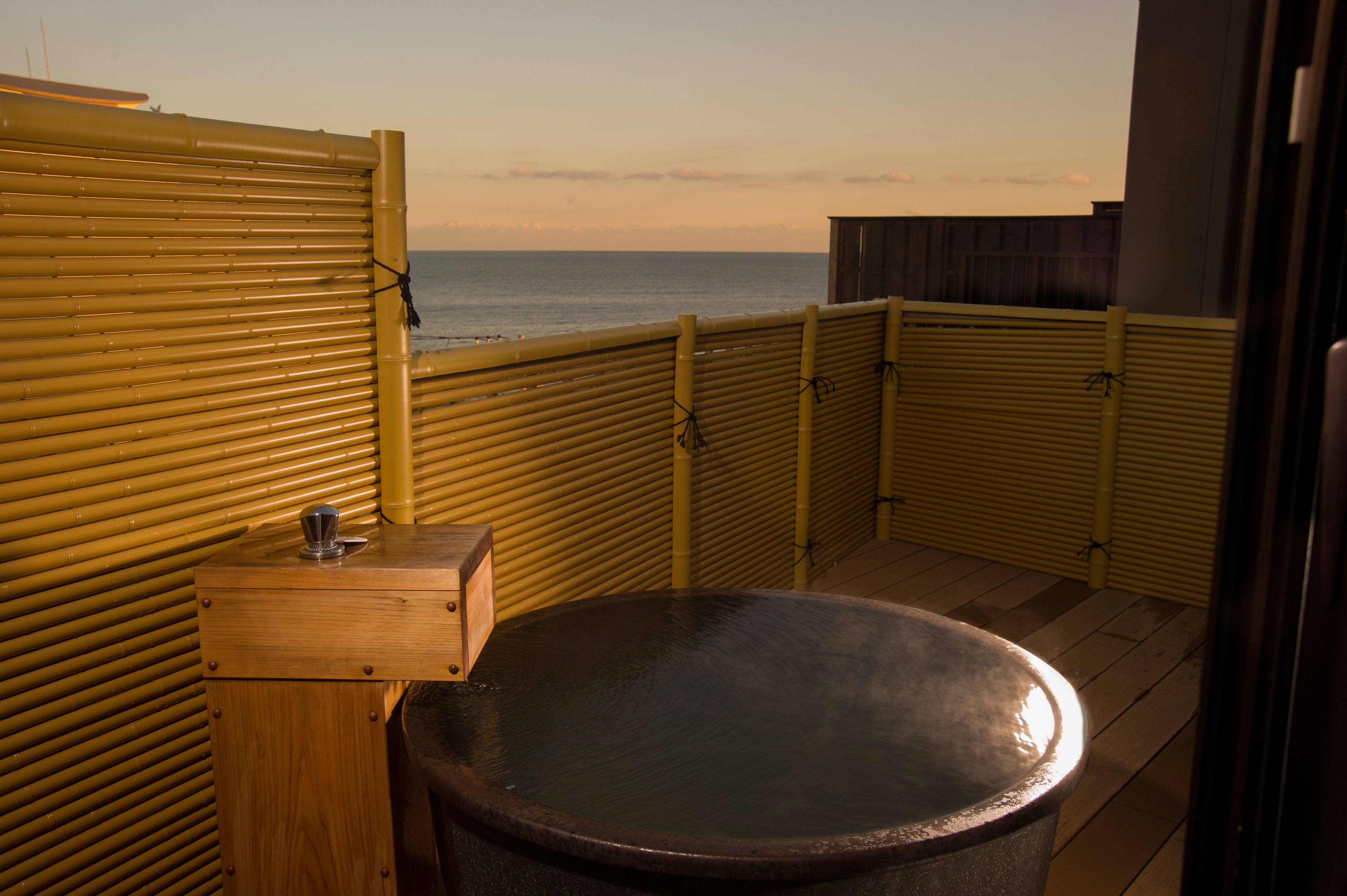 Una bañera de madera con vista al mar, un banco de madera y una valla de bambú.
