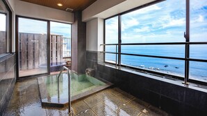 A modern bathroom with a glass-enclosed hot tub, large windows with ocean views, and a wooden ceiling.