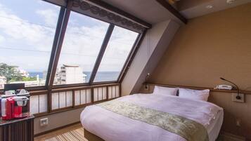 A hotel room with a large window, a bed, a bedside table with a phone, and a view of the city and sea.