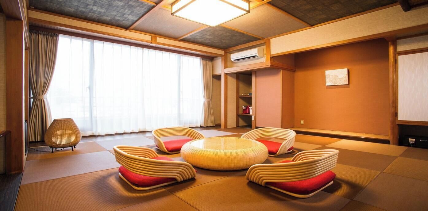 Una habitación con suelo de tatami, una zona de estar circular en el centro y un amplio ventanal con cortinas.