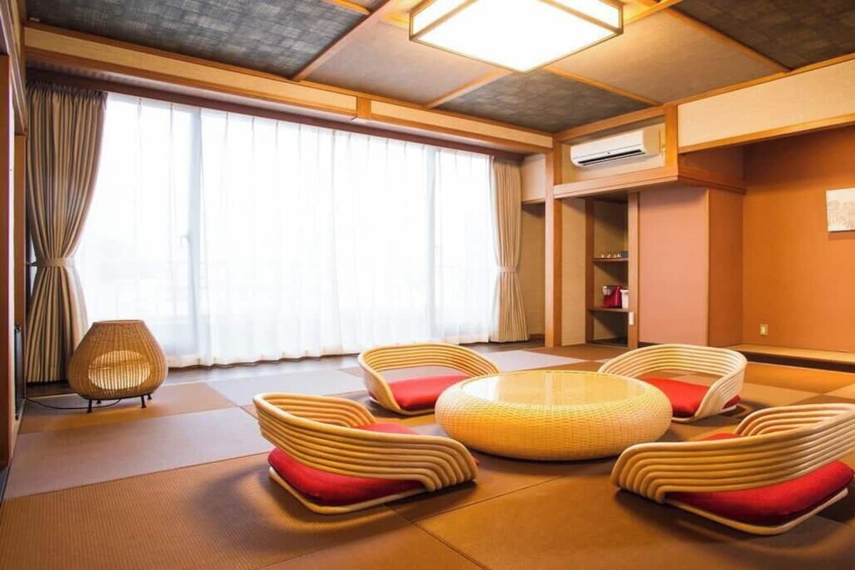 Una habitación con suelo de tatami, una zona de estar circular en el centro y un amplio ventanal con cortinas.