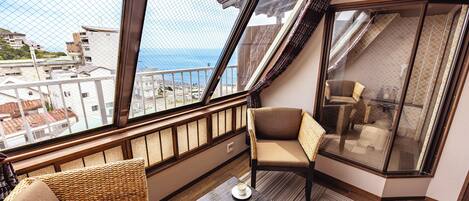 A balcony with a view of the sea, wicker furniture, and a glass door leading to a bathroom.