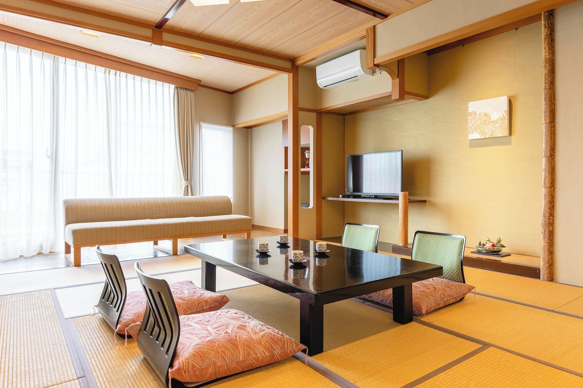 Una habitación tradicional japonesa con suelo de tatami, una mesa baja, cojines, un sofá y un televisor.