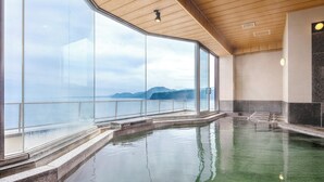 An indoor swimming pool with large windows offering a view of the sea and mountains.