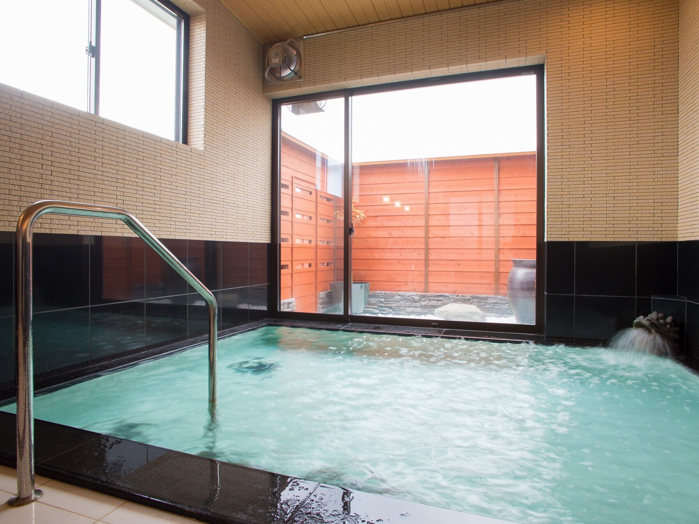 Un espace bien-être comprenant un jacuzzi, une porte vitrée donnant sur l’extérieur et une vue sur un bâtiment en briques.