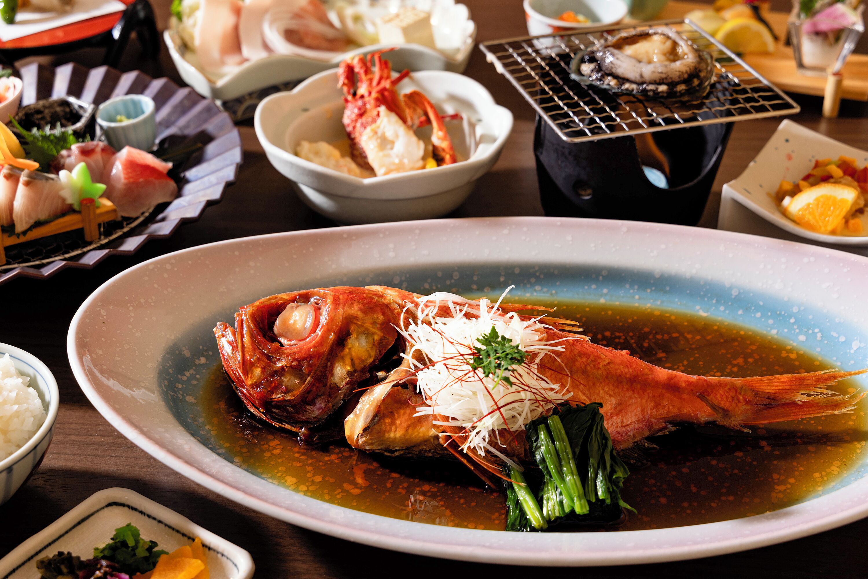 A variety of dishes including a prominent bowl of seafood with a sauce, surrounded by other bowls of food and a grill.