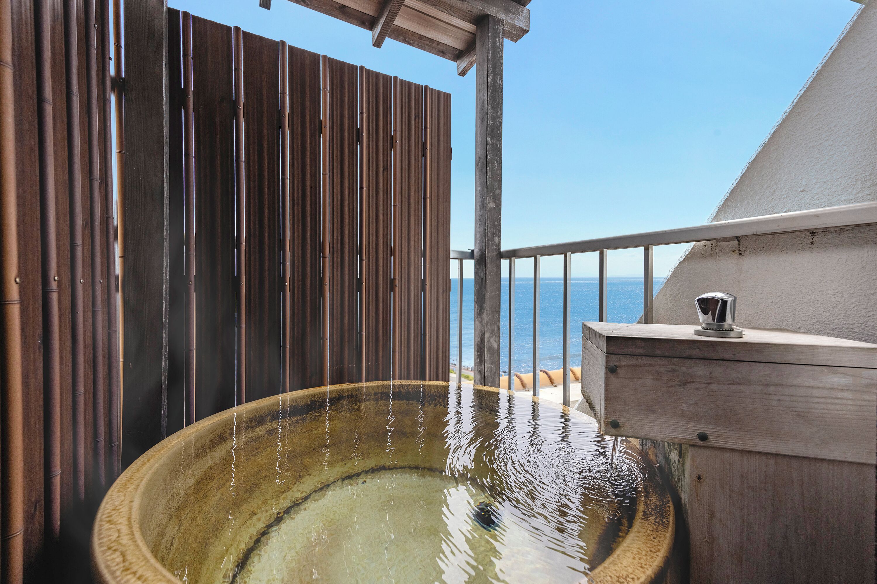 Una bañera de hidromasaje con agua fluyendo, una valla de madera y vista al mar.