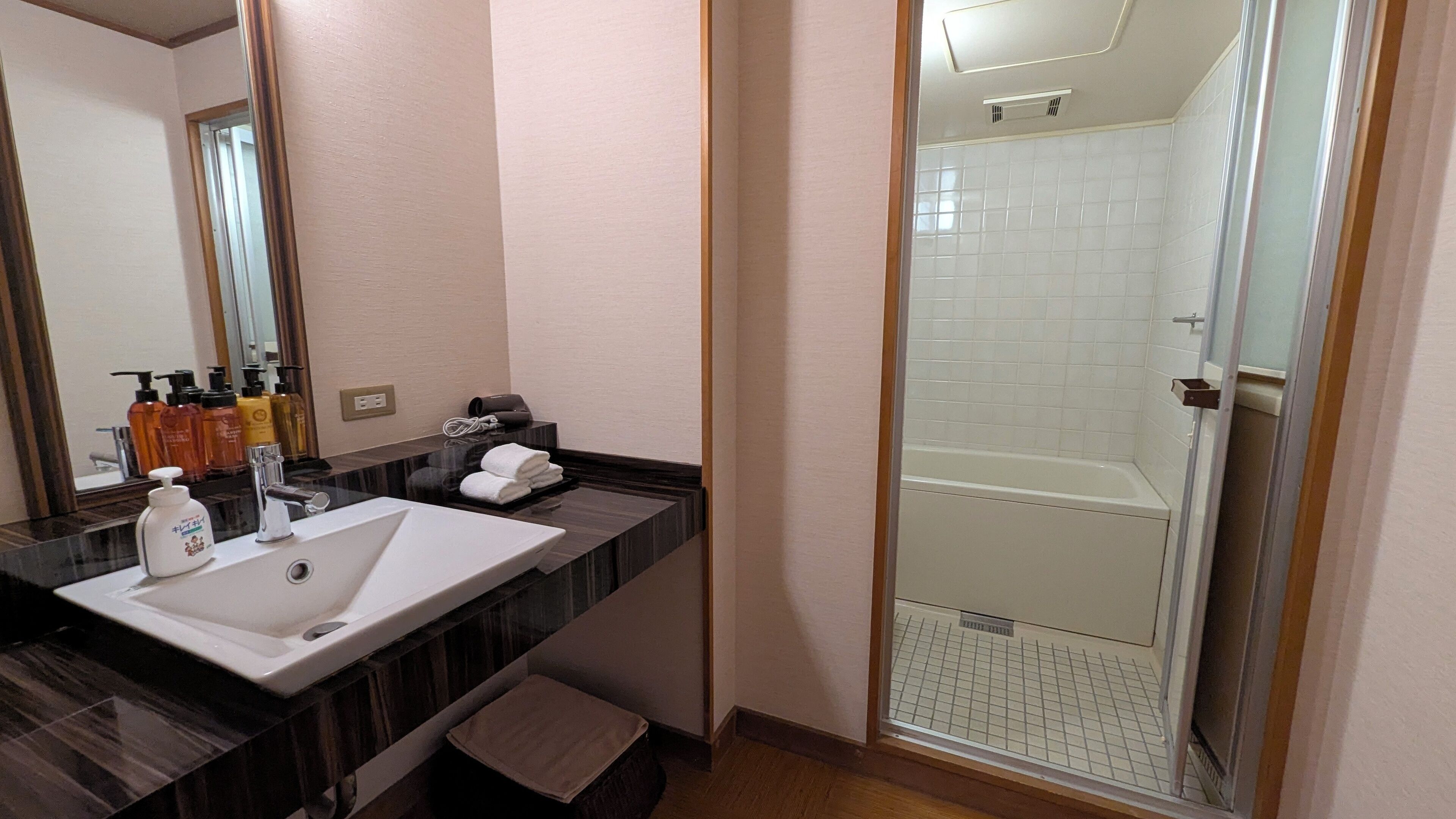 Un baño con lavamanos blanco, encimera de mármol oscuro y cabina de ducha con mampara de vidrio.