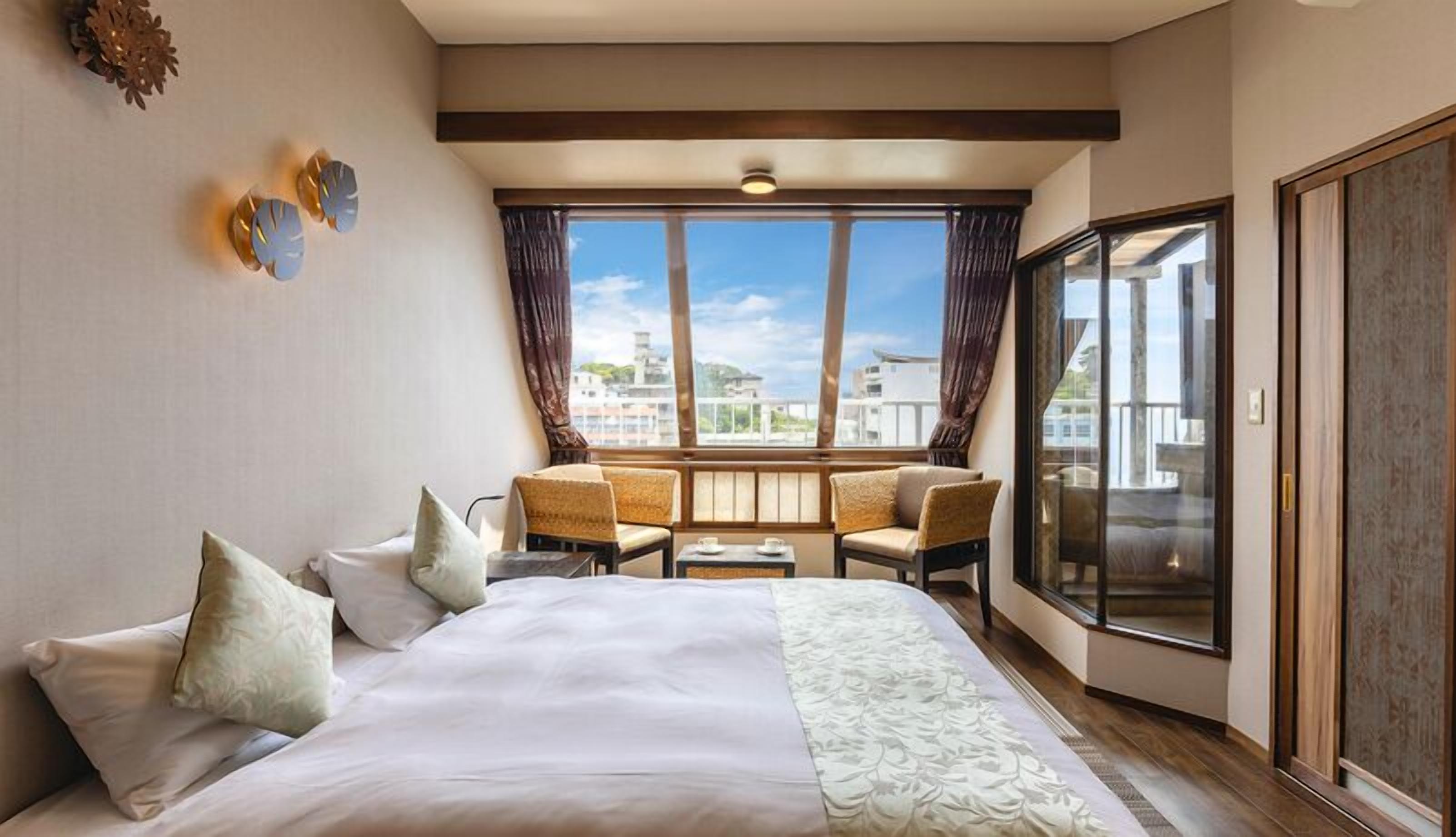 Habitación de hotel con una cama grande, un balcón con vistas y un área de estar con sillas y una mesa.