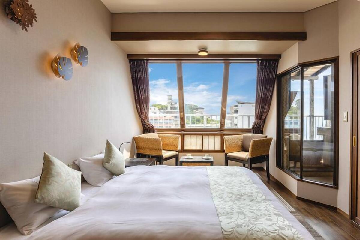 Habitación de hotel con una cama grande, un balcón con vistas y un área de estar con sillas y una mesa.