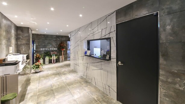 Una hall d'albergo moderna con una reception, una porta nera e una parete in marmo con un orologio.