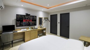Una camera d'albergo moderna con una grande TV che mostra Netflix, una scrivania con un computer, un letto e due armadi.