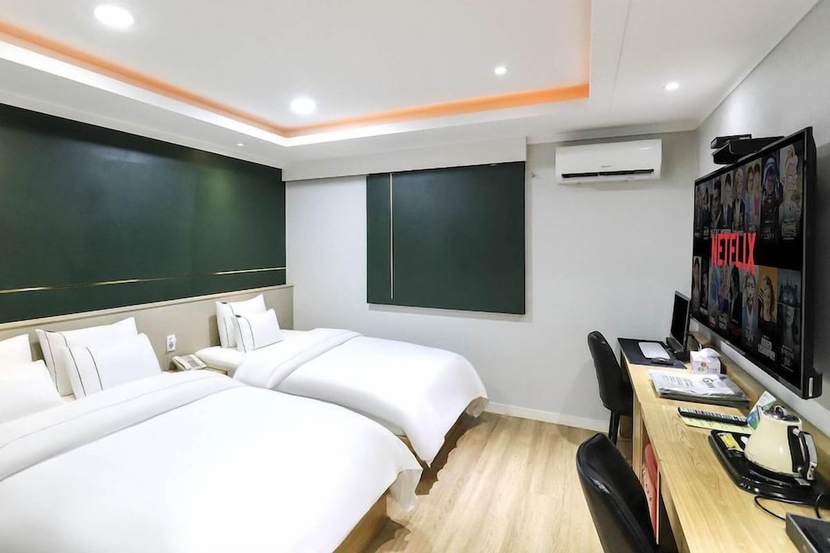 A hotel room with two beds, a desk with a computer, and a wall-mounted TV.