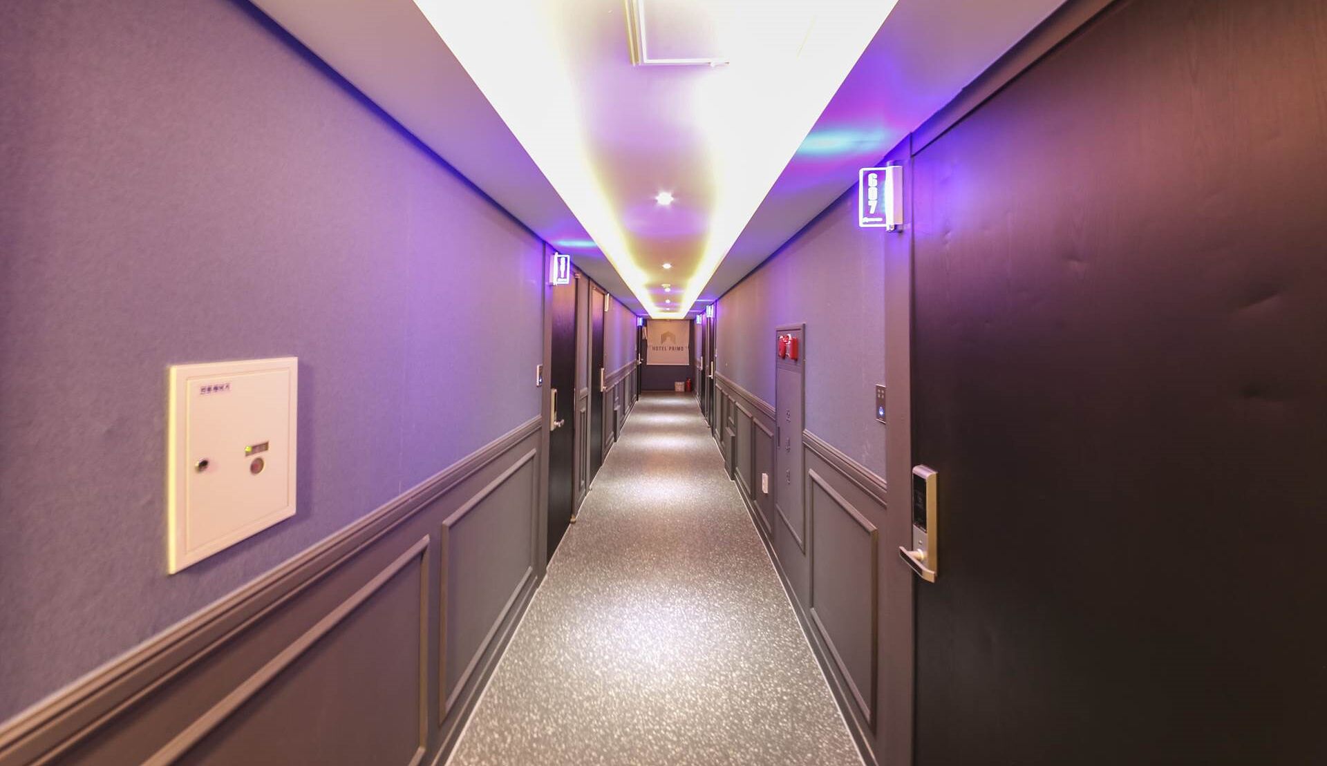 Un couloir d’hôtel aux murs violets, doté d’un sol recouvert de moquette et d’un panneau indiquant le numéro de chambre 617.