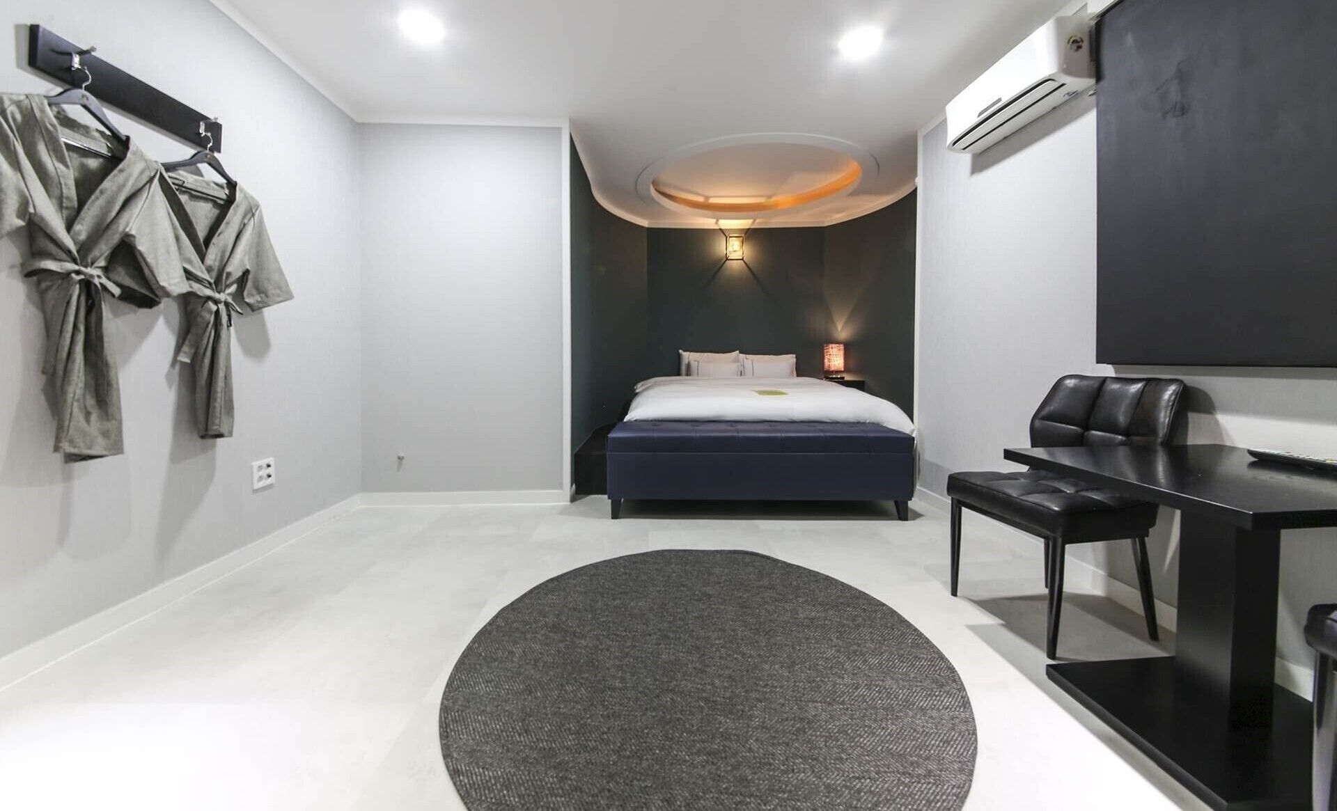 A modern hotel room with a large bed, a desk, a chair, and a robe rack.