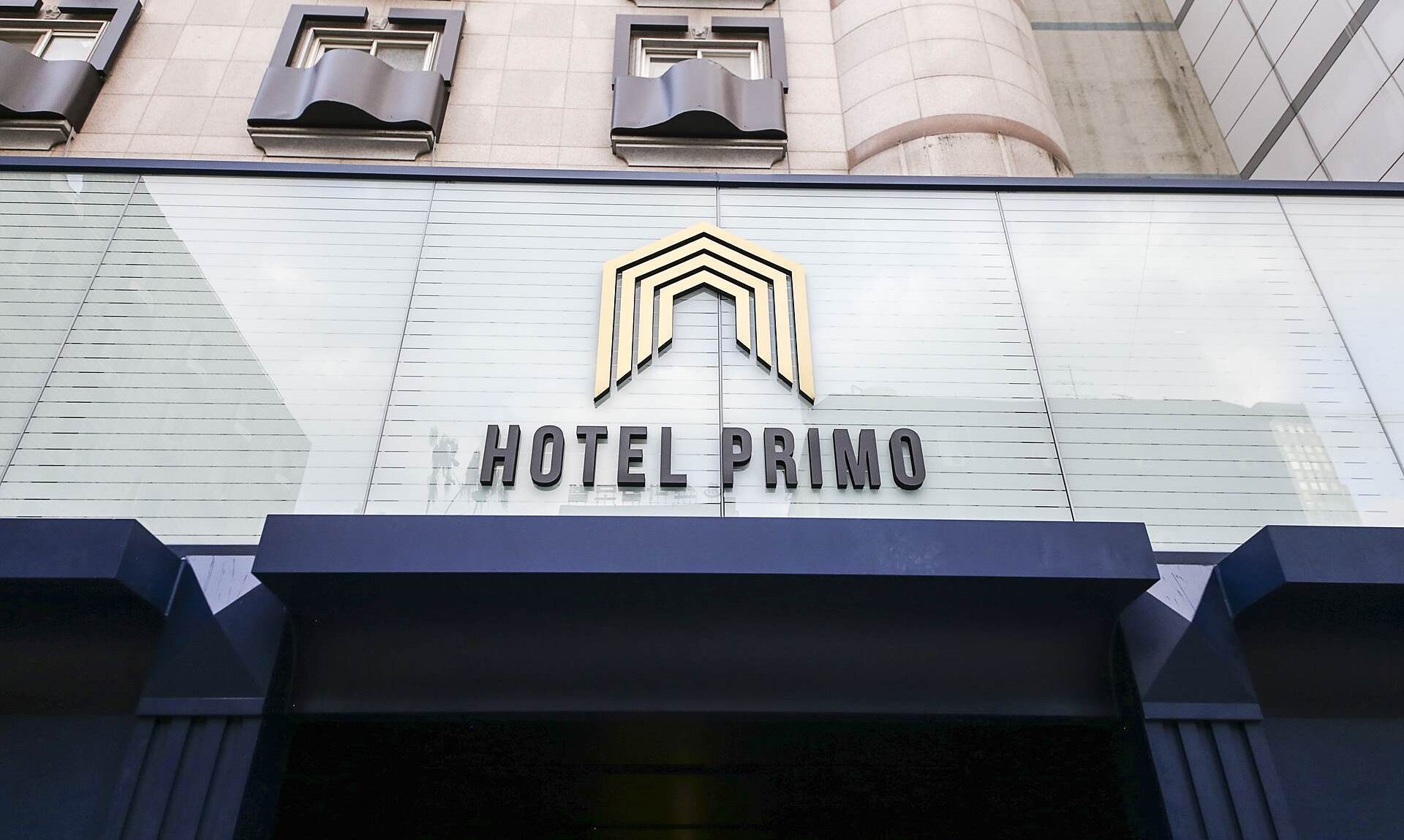 The exterior of Hotel Primo with a modern design, featuring a prominent logo and the name displayed on the facade.