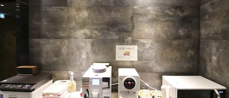 A kitchen area with a microwave, a coffee machine, and a food display.