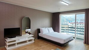 Habitación de hotel con cama, televisión y vistas a edificios a través de un gran ventanal.