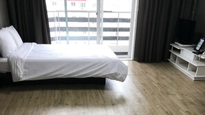 Una habitación de hotel con cama, suelo de madera, un mueble para televisión y vistas a través de una ventana.