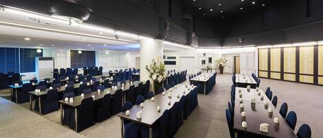 A conference room with multiple tables and chairs, arranged in rows, with a carpeted floor and a ceiling with recessed lighting.