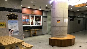 Un interior moderno y limpio con un banco de madera, un pilar central y una barra con un menú.