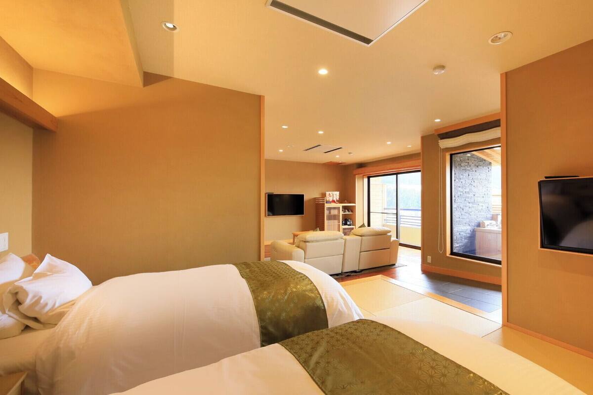 Habitación de hotel con cama, televisión, sofá y un amplio ventanal.