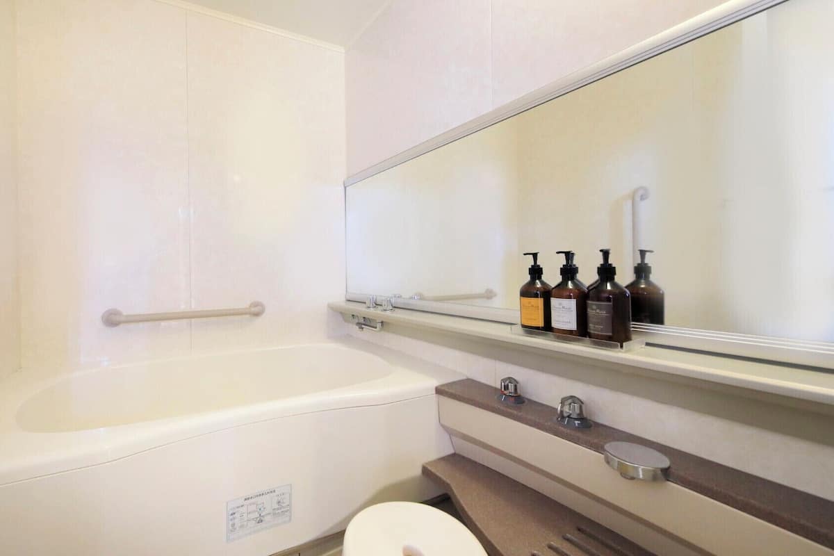 Un baño con bañera, inodoro, lavabo, espejo y estante con artículos de aseo.