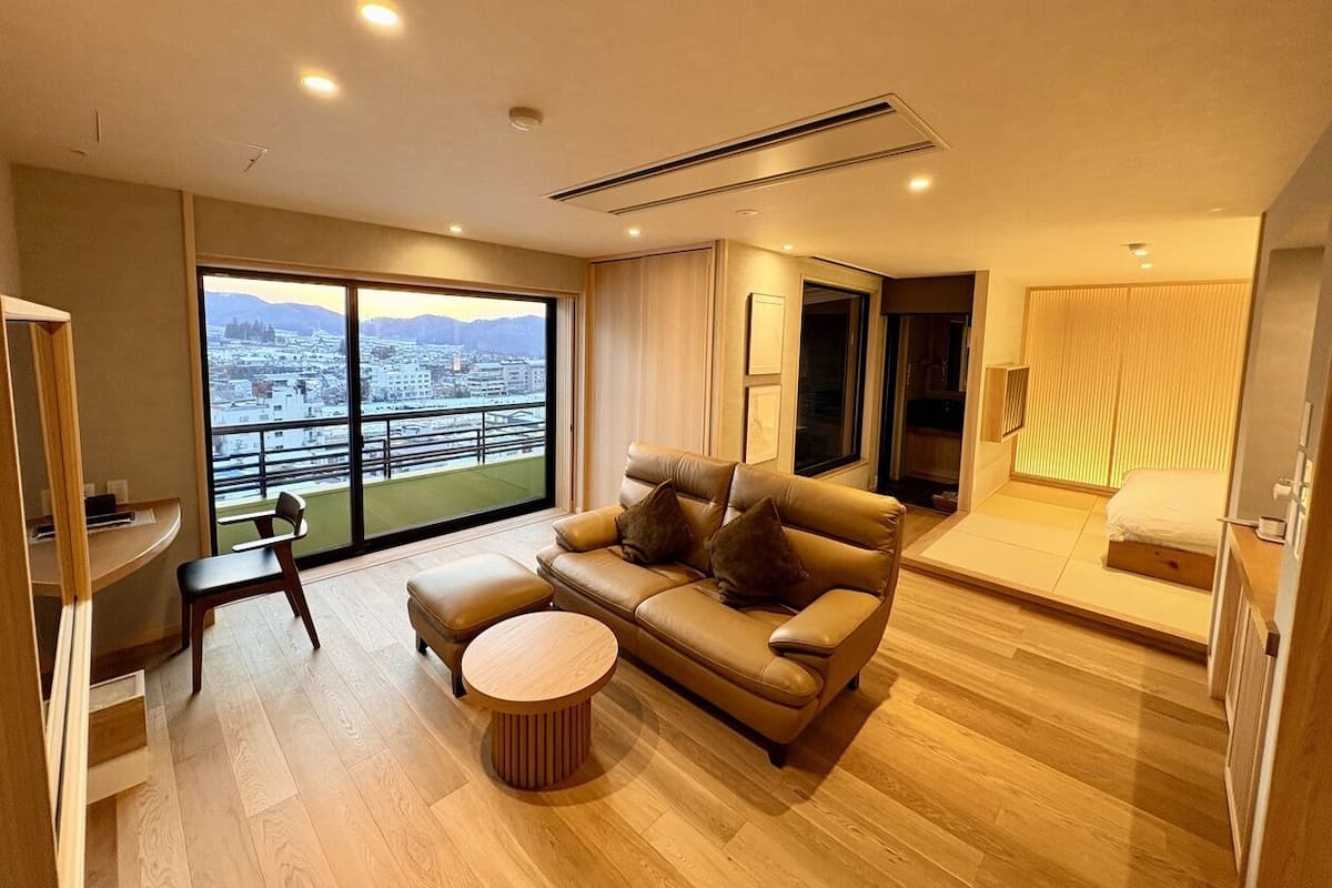 Una sala de estar moderna con un sofá, una mesita redonda y vistas de un paisaje urbano a través de amplios ventanales.