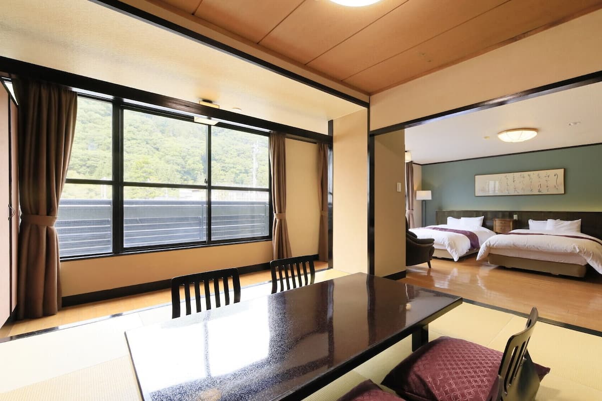 Una habitación de hotel con un ventanal grande, una cama, una mesita de noche y una silla.