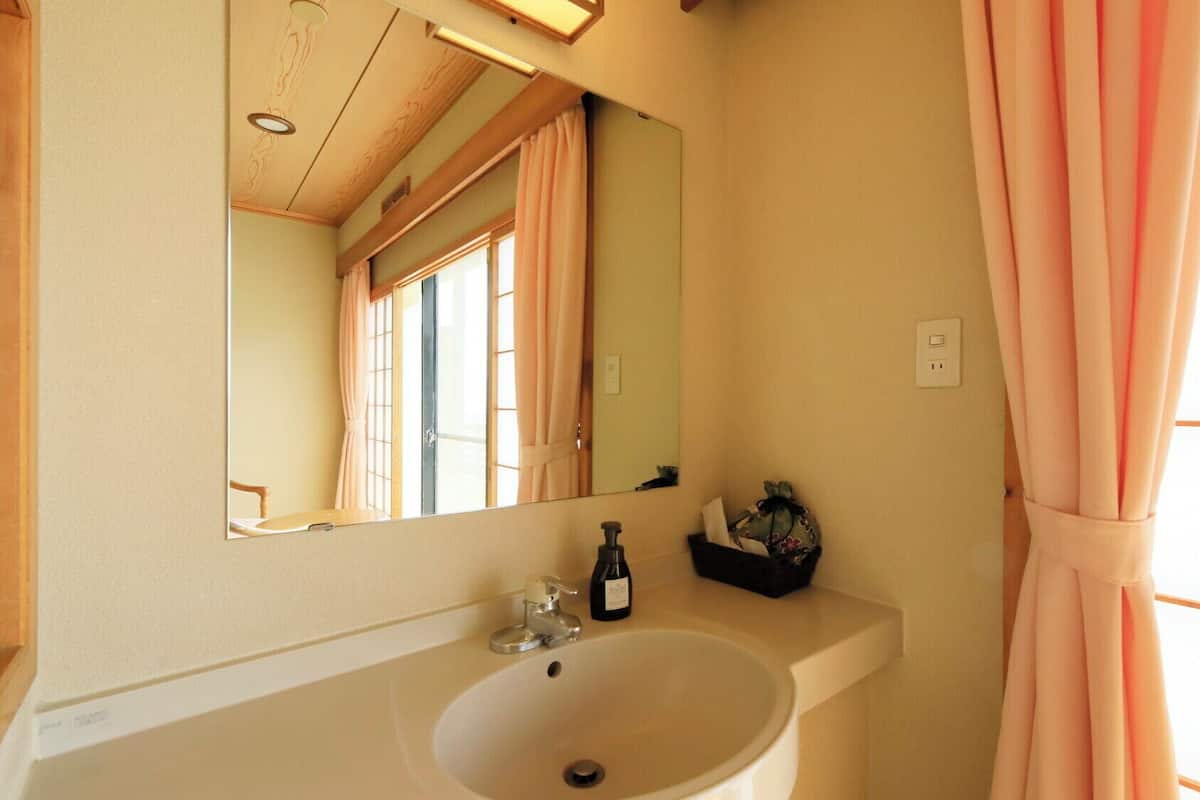Un baño con lavamanos, espejo y ventana con cortinas.