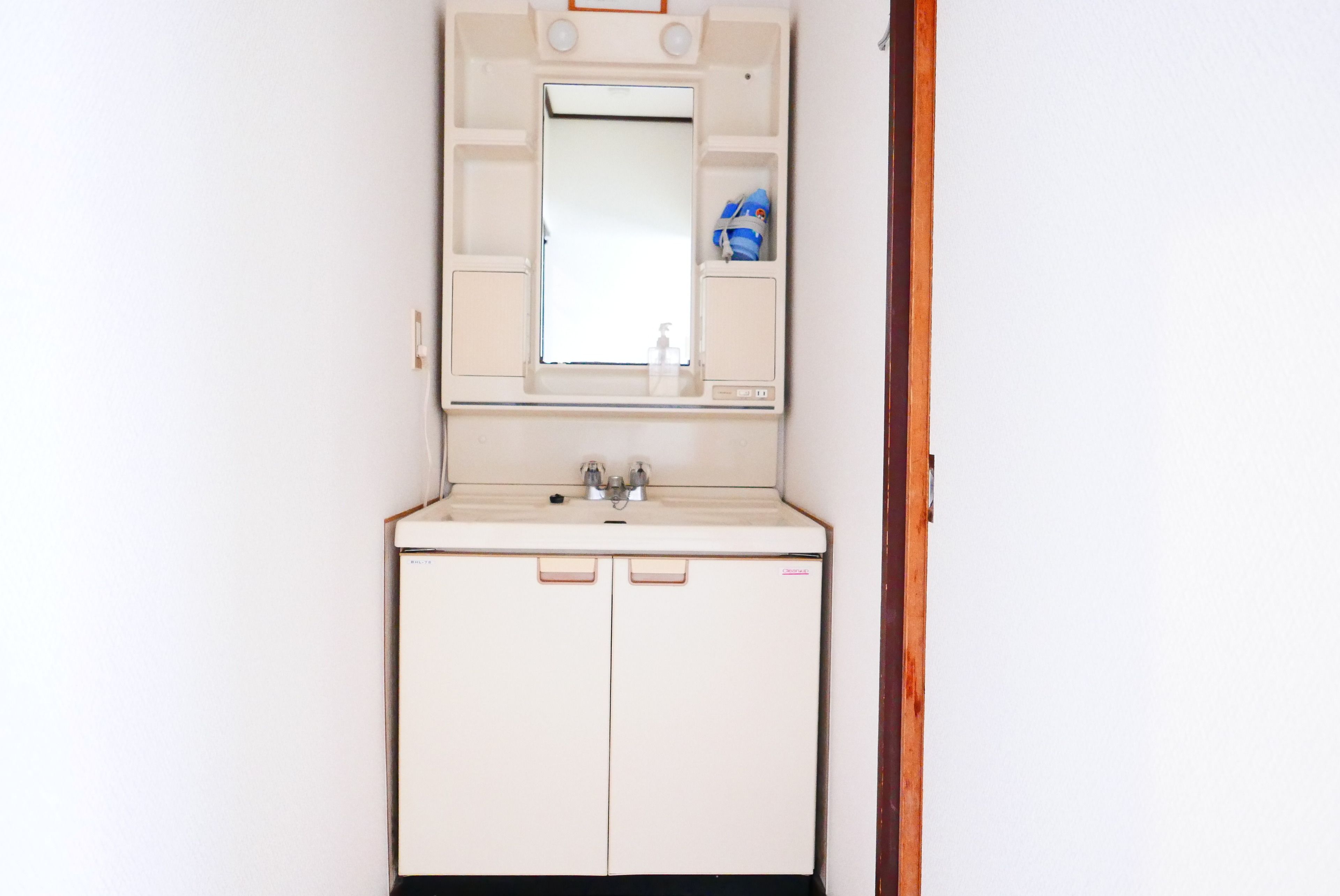 A small, white bathroom with a mirror, sink, and two cabinets.